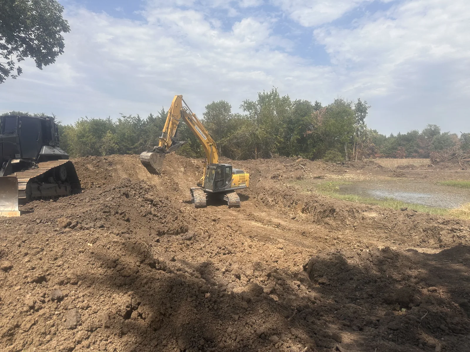 Excavator and dozer working the pond bank with water showing behind