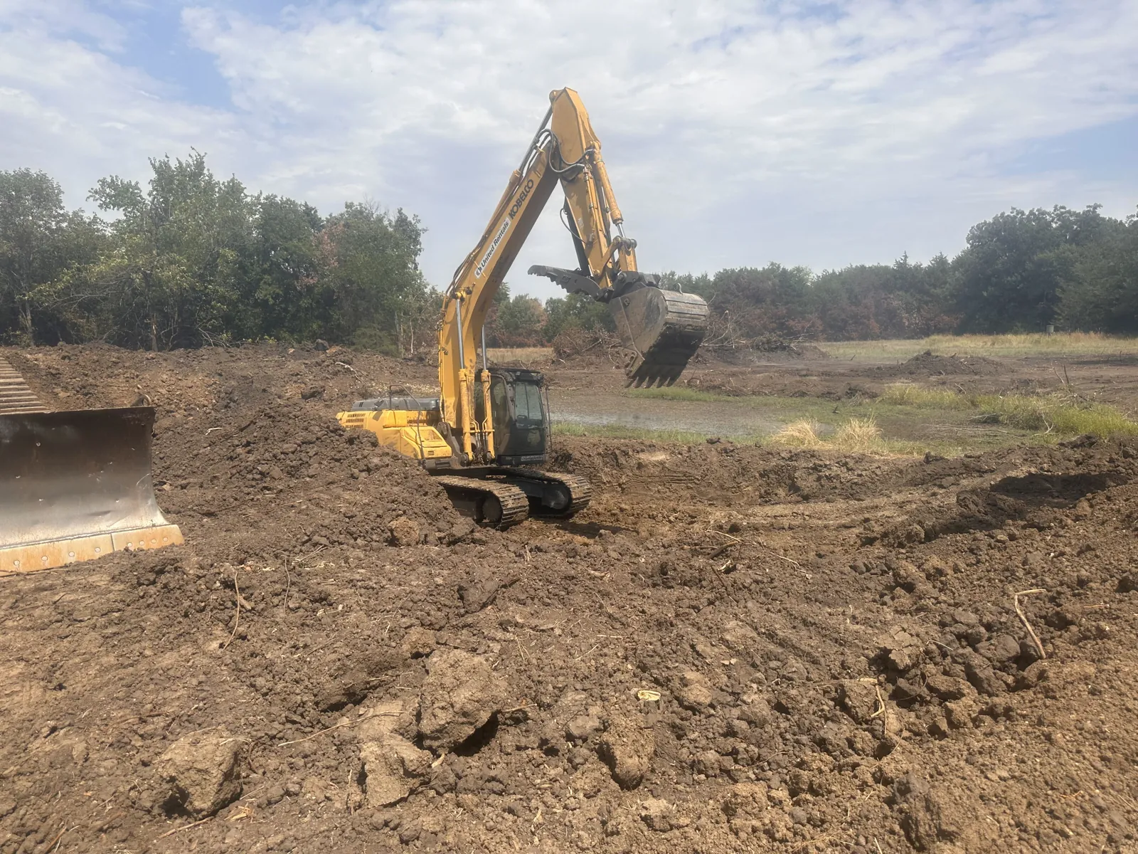 Excavator digging a pit on an Oklahoma ranch job with the spoil piled beside it
