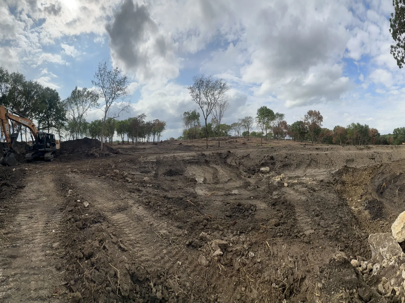 Wide view of the excavator digging the pond basin