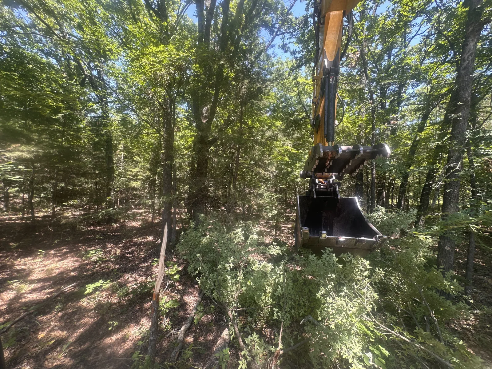 Excavator working in cross timbers ground where a pond site is being opened up