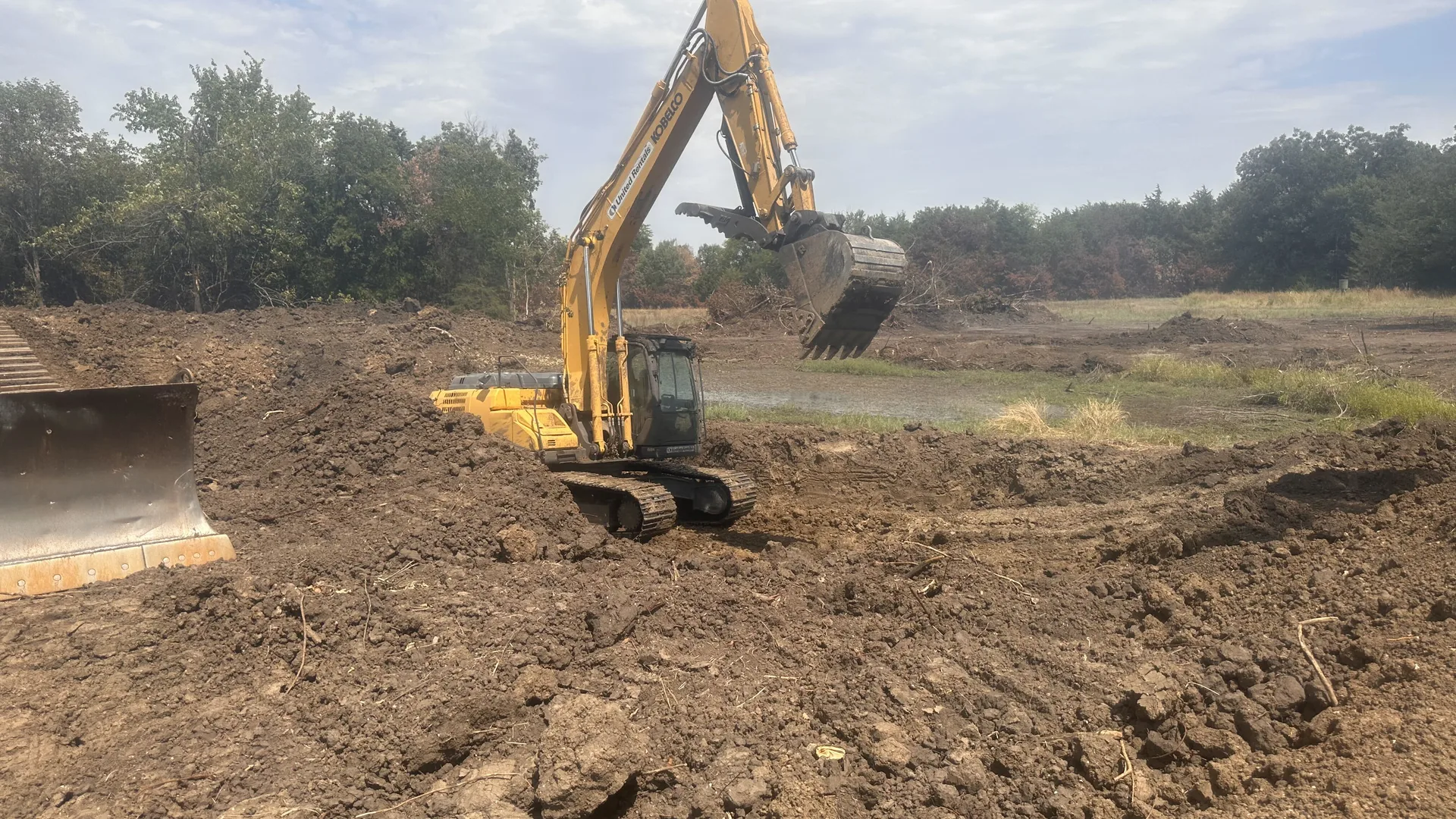 Excavator shaping the pond bank beside the dozer blade